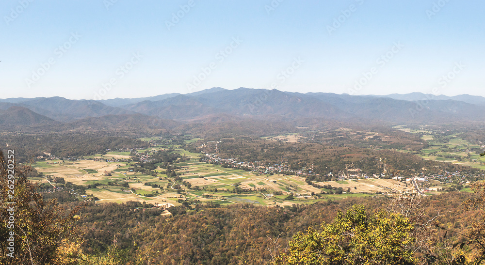 Landscape nature of rice field and small town valley in middle hill and trees in foreground with blue sky background.