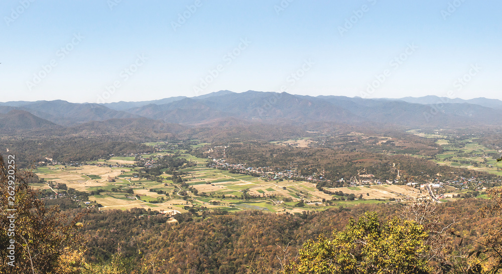 Obraz premium Landscape nature of rice field and small town valley in middle hill and trees in foreground with blue sky background.