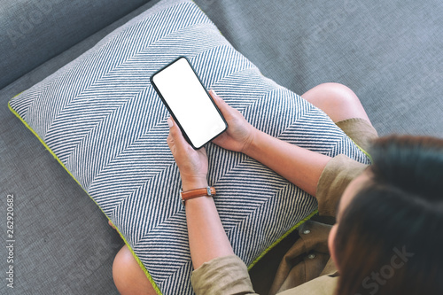 Top view image of a woman holding black mobile phone with blank white desktop screen while sitting in living room with feeling relaxed