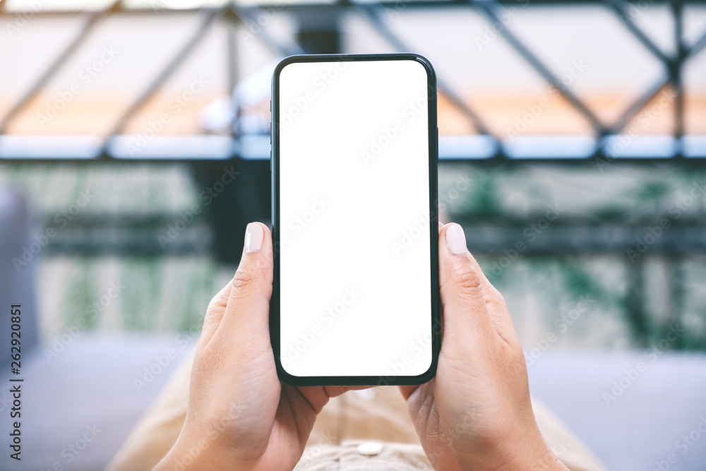 Mockup image of a woman holding black mobile phone with blank white desktop screen while laying down in living room with feeling relaxed Mockup image of a woman holding black mobile phone with blank white desktop screen while laying down in living room with feeling relaxed