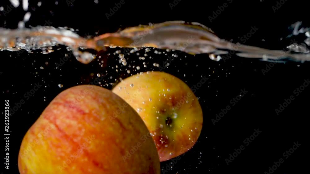 Two red apples falling into water in front of a black background in slow motion. Two red apples falling into water in front of a black background in slow motion.