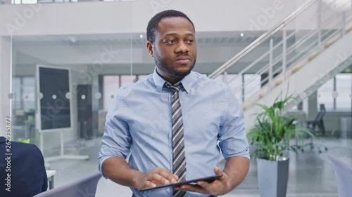Handsome Young Black Manager in a Shirt Walking Pass His Business Colleagues with a Tablet and Supervise Their Work. Diverse and Motivated Business People Work on Computers in Modern Open Office.