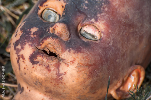 Creepy old doll head. Broken abandoned damaged scary toy in a garbage dump close-up. In the toy  the eye and mouth are damaged. The concept of fear  horror  crime. Very scary.