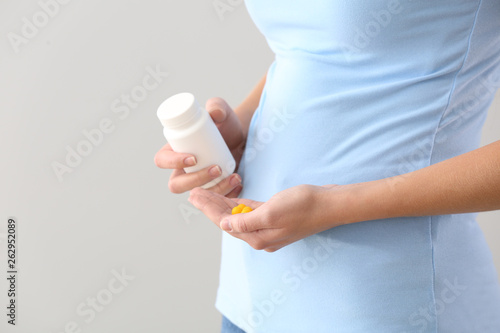 Pregnant woman with vitamins on light background, closeup