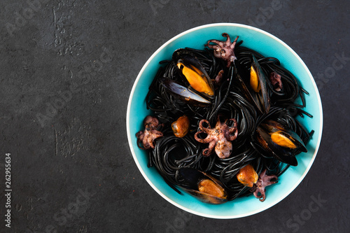 Top view of mediterranean black pasta with seafood. Spaghetti Nera with cuttlefish ink, mussels, shrimp and red chili pepper on blue plate. on dark background.