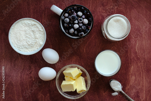 Ingredients for cooking berry pie. Eggs, sugar, milk, butter, flour, currants on a wooden table. Rustik style. Top view.