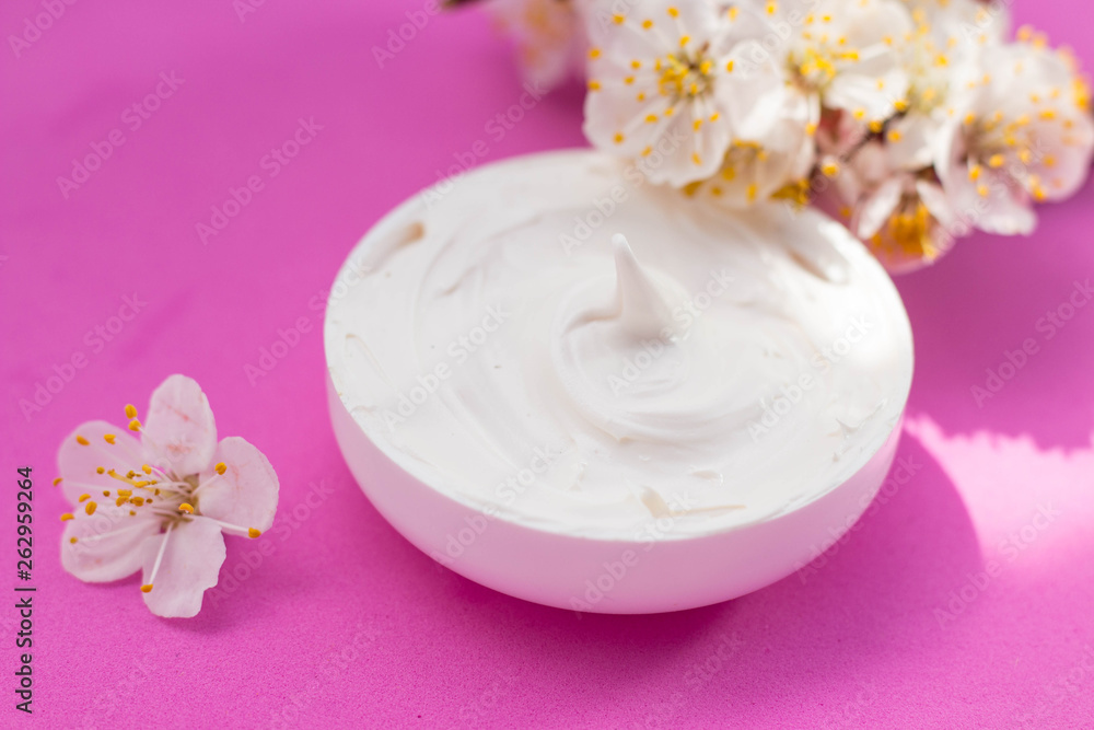 face cream and apricot flowers pink background