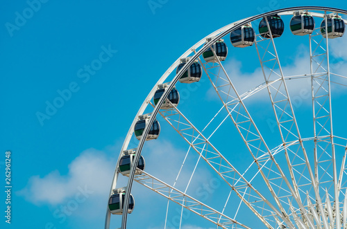 Closeup modern Ferris wheel against blue sky and white clouds. Ferris wheel at funfair for entertainment and recreation on holiday. Modern construction of Ferris wheel in amusement. Fun festival.