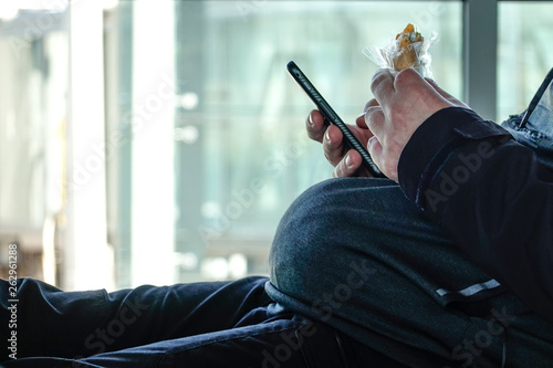 Riga, Latvia An overwight man eating while looking at his mobile phone. photo