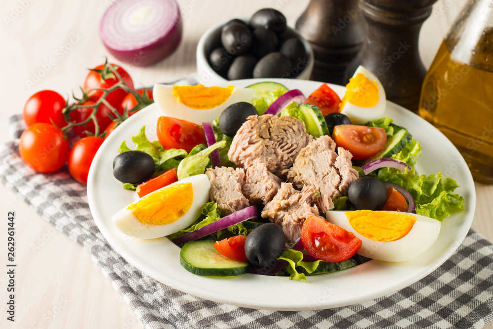 Fresh Caesar tuna salad with delicious tuna fish, ruccola, spinach, cabbage, arugula, egg, parmesan and cherry tomato on wooden background. Oil, salt and pepper. Healthy and diet food concept. Fresh Caesar tuna salad with delicious tuna fish, ruccola, spinach, cabbage, arugula, egg, parmesan and cherry tomato on wooden background. Oil, salt and pepper. Healthy and diet food concept.