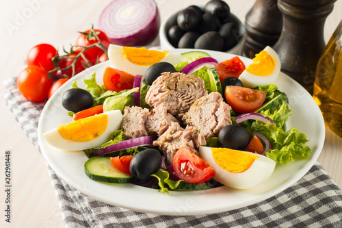 Fresh Caesar tuna salad with delicious tuna fish, ruccola, spinach, cabbage, arugula, egg, parmesan and cherry tomato on wooden background. Oil, salt and pepper. Healthy and diet food concept.