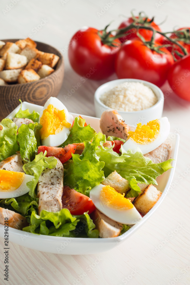 Fresh Caesar salad with delicious chicken breast, ruccola, spinach, cabbage, arugula, egg, parmesan and cherry tomato on wooden background. Oil, salt and pepper. Healthy and diet food concept. Fresh Caesar salad with delicious chicken breast, ruccola, spinach, cabbage, arugula, egg, parmesan and cherry tomato on wooden background. Oil, salt and pepper. Healthy and diet food concept.