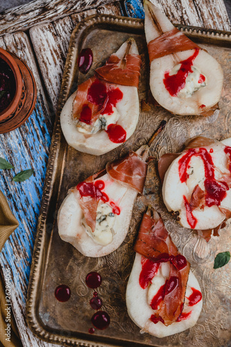 baked pears with blue cheese and prosciutto ham in bowl  with lemons. grape and textile on wooden background photo