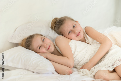 Two little six years old sisters in the bed lay on the pillows