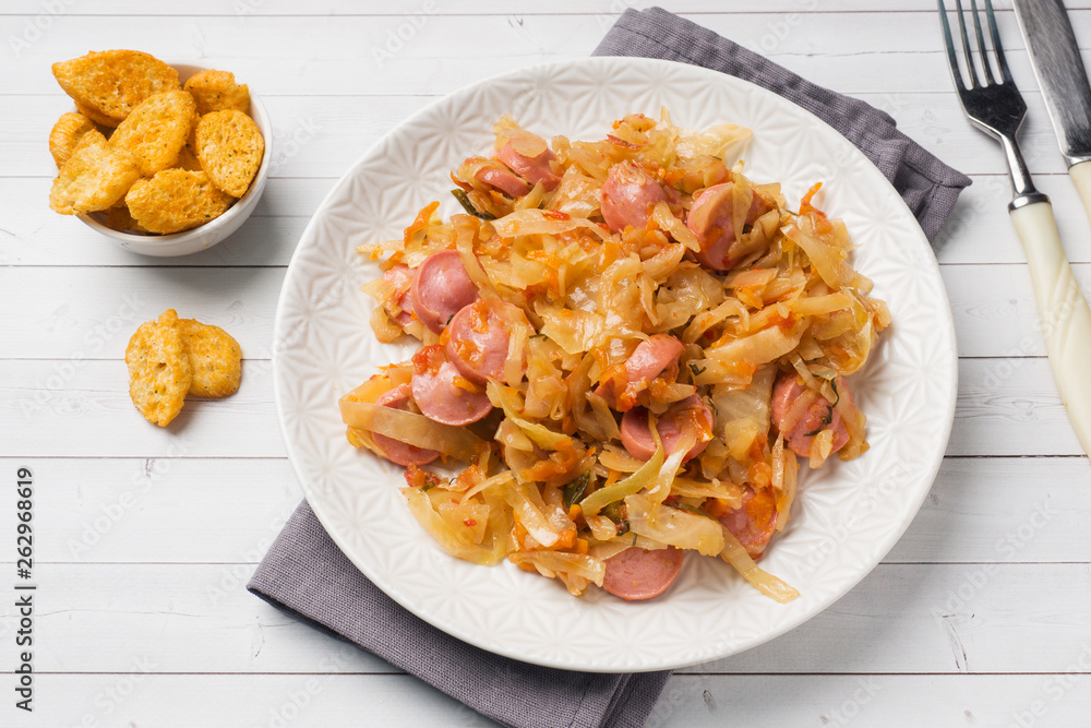 Stewed cabbage with sausages in a plate on the table. Selective focus.