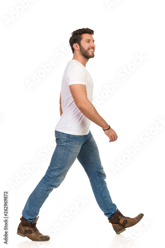 Young Man In Jeans And White T-shirt Is Walking And Looking Up. Side View