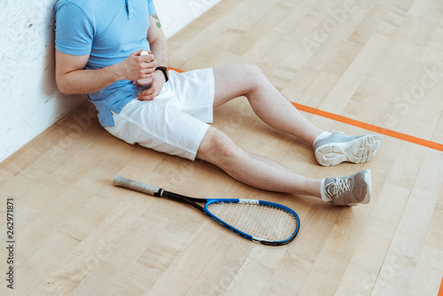 Cropped view of squash player sitting on floor and holding bottle of water