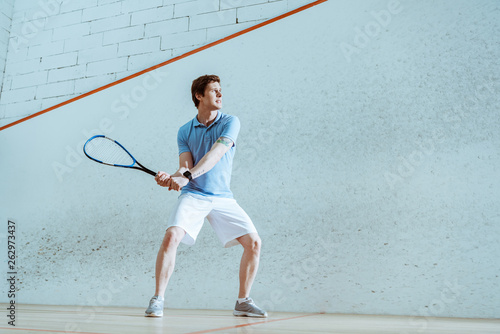 Full length view of concentrated sportsman in blue polo shirt playing squash