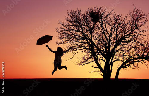 Silhouette of a girl with an umbrella on the background of a beautiful sunset, the girl is flying on an umbrella, jumping up