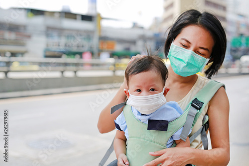 Asian mother carrying her infant baby by hipseat outdoor with wearing a protection mask against PM 2.5 air pollution in Bangkok city. Thailand.