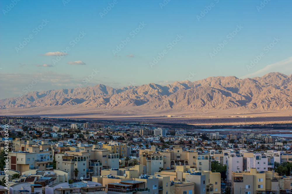 Middle East small city in desert with bare wilderness mountain ridge background in sand stone dunes scenic landscape