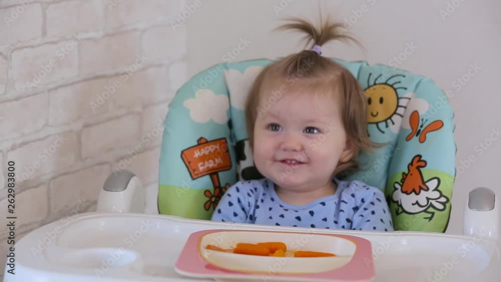 A little girl sitting on a high chair and eating different vegetables and fruits A little girl sitting on a high chair and eating different vegetables and fruits