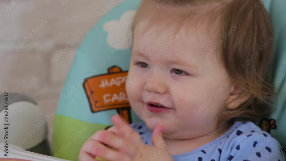 A little girl sitting on a high chair and eating different vegetables and fruits A little girl sitting on a high chair and eating different vegetables and fruits