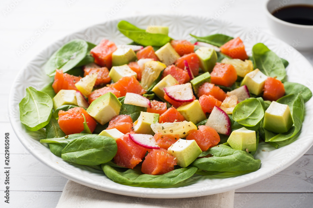 Poke Hawaiian salad with salmon, avocado spinach and vegetables in a plate on a white table.