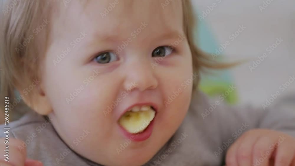 A little girl sitting on a high chair and eating different vegetables and fruits A little girl sitting on a high chair and eating different vegetables and fruits