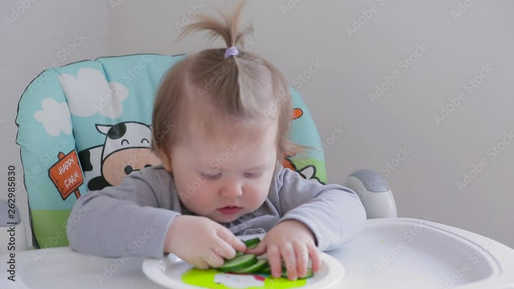A little girl sitting on a high chair and eating different vegetables and fruits A little girl sitting on a high chair and eating different vegetables and fruits