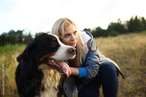 Young woman walking with Bernese Mountain Dog on the summer field