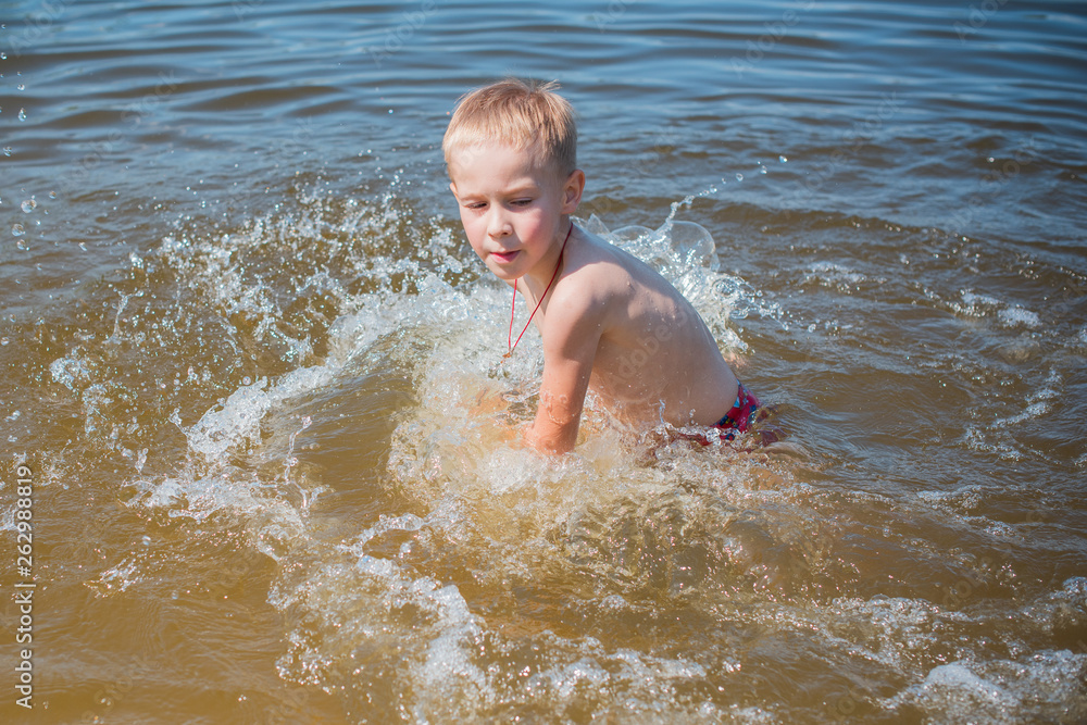 Boy  playing on the beach on summer holidays. Children in nature with beautiful sea, sand and blue sky. Happy kids on vacations at seaside in the water 