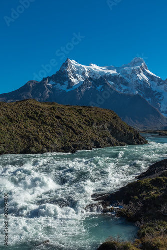 Waterfall cascading with a thunderous roar with a mountain range in the background, Torres del Paine, National Park, Chile, clear blue sky, portrait aspect © Wise Dog Studios