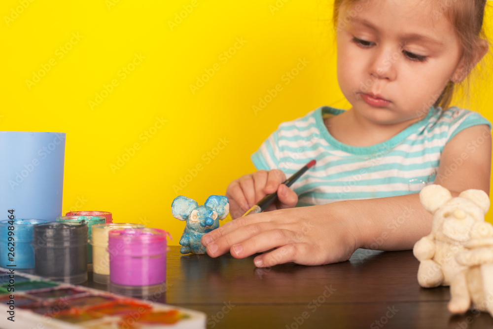 Little girl paints toy animals paints on a yellow background Little girl paints toy animals paints on a yellow background