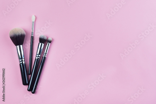 Set of flat top view of various professional female cosmetics brushes for makeup isolated on pink background with copy space.