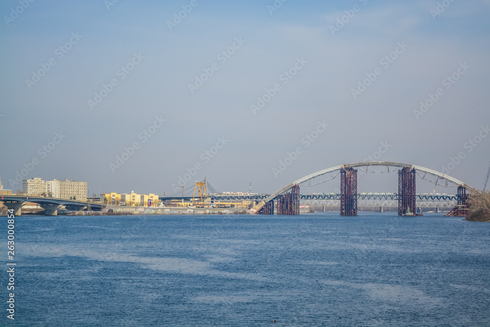 Naklejka premium View of Dnieper river and the bridge from the coast of Kiev. Modern big city. Beautiful spring landscape