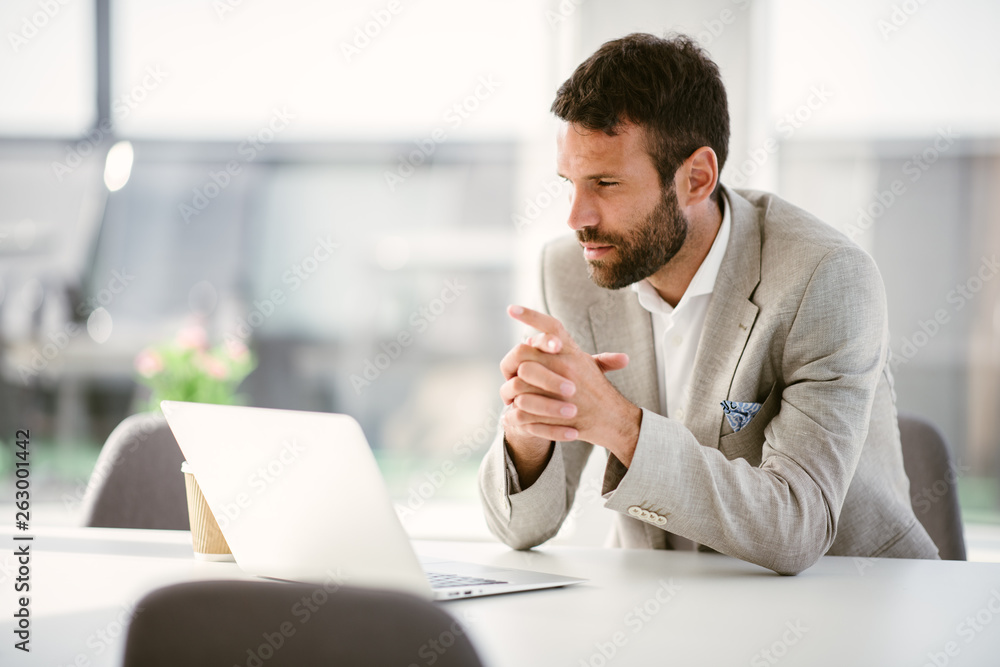 Businessman sitting looking at his laptop. Businessman working in the office on his laptop. Stylish businessman working on a project in the office thinking about future Businessman sitting looking at his laptop. Businessman working in the office on his laptop. Stylish businessman working on a project in the office thinking about future