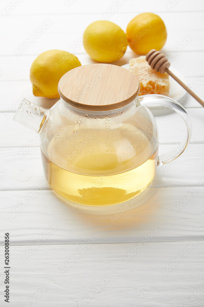 transparent teapot with green tea, lemons and honeycomb on white wooden table transparent teapot with green tea, lemons and honeycomb on white wooden table