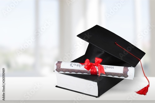 Graduation mortarboard on top of stack of books on background