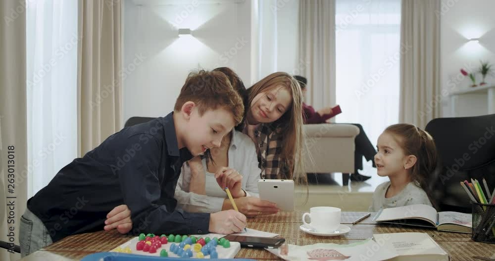 Happy and smiling mother helping her kids on a school project they using a tablet to resolve a problem at the end they get the right results happy hugging each other. 4k Happy and smiling mother helping her kids on a school project they using a tablet to resolve a problem at the end they get the right results happy hugging each other. 4k
