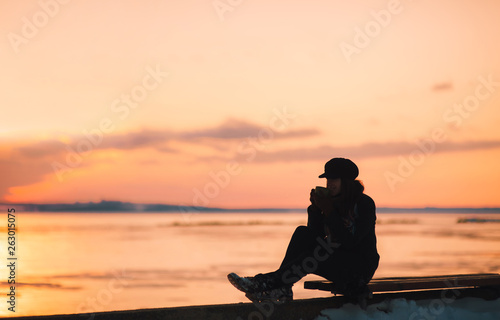 Beautiful girl is drinking hot tea from the thermos for a walk. How to warm up in winter or autumn and overcome depression.