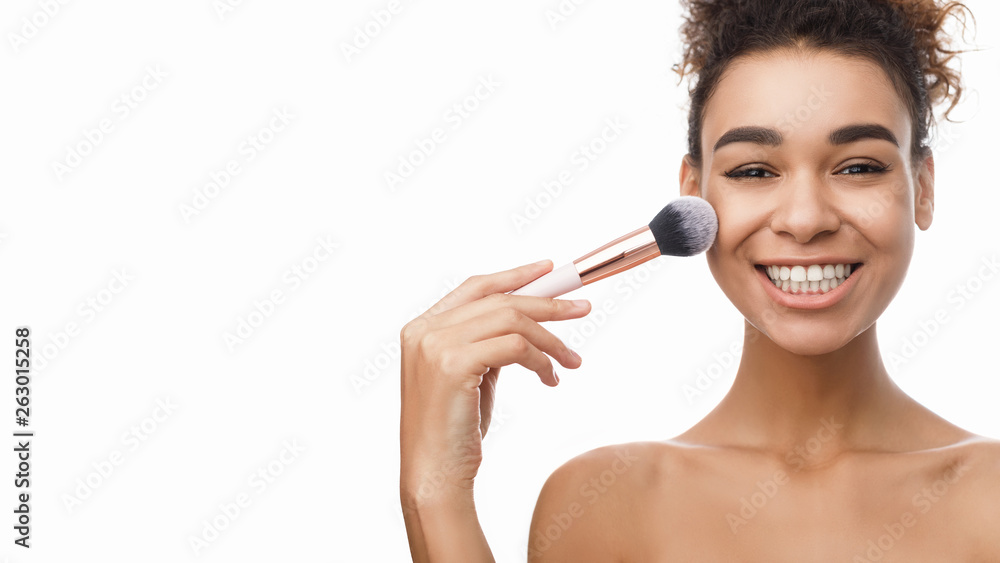 African-american woman applying blush on face with brush tool African-american woman applying blush on face with brush tool
