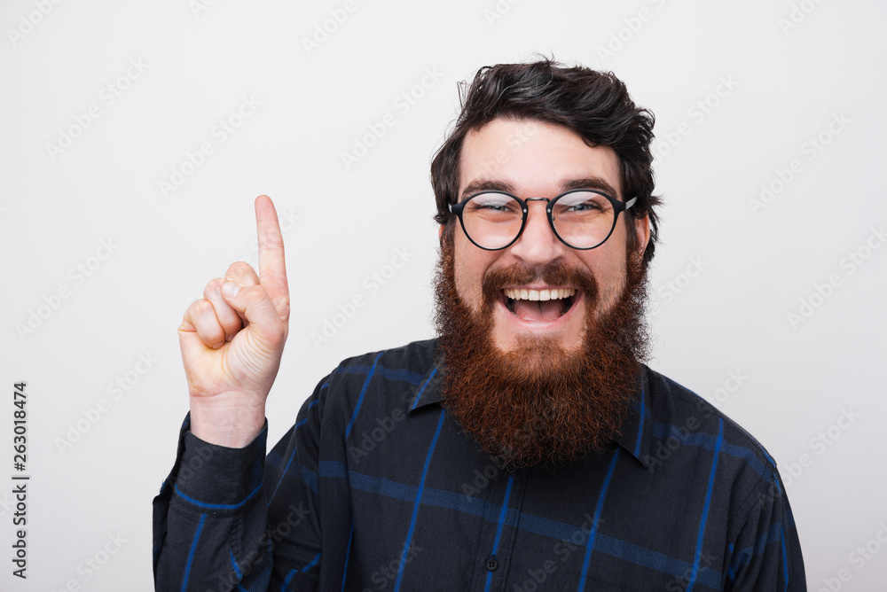 Portrait of happy cheerful bearded man wearing glasses and pointing up over white background Portrait of happy cheerful bearded man wearing glasses and pointing up over white background