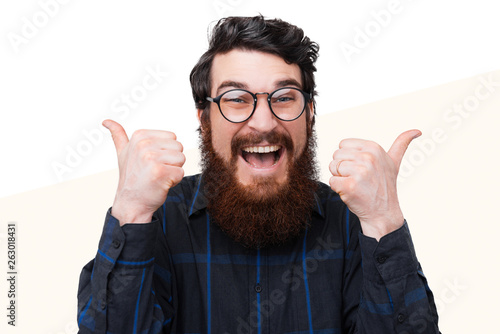 Amazed and excited bearded man in casual showing thums up over white background photo