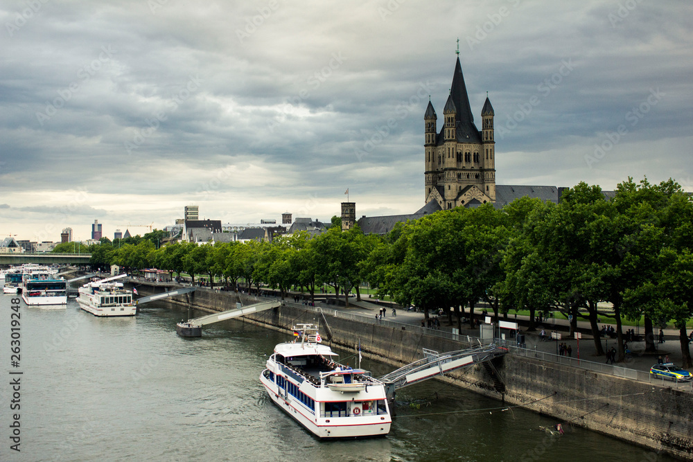 Picturesque view of Cologne central part of city in Germany across the Rhine river. The Great Saint Martin Church on the other side of Rhine. Moored cruise liners and boats on the river Rhine bank.