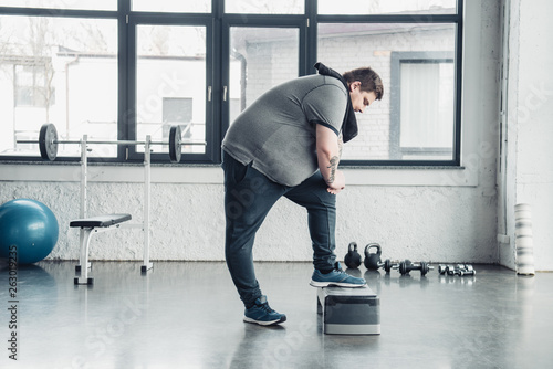 overweight man with towel exercising on step platform at sports center