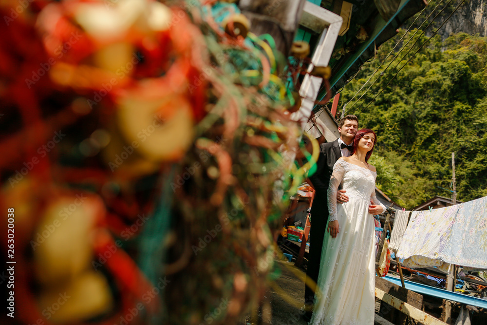 Happy cheerful wedding couple posing on dock near houses