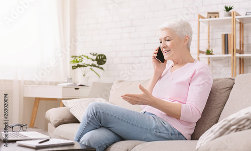 Cheerful senior woman talking with client oh phone
