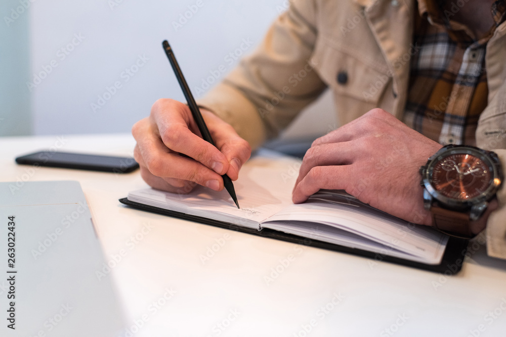 Cropped view of man writing in notebook at table Cropped view of man writing in notebook at table