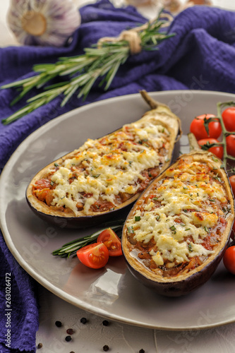 Baked eggplants with roasted meat, tomatoes and cheese. Traditional dish of the Balkan cuisine. A large portion on a plate and a blue napkin on a light background. Ketogenic food. Vertical view.